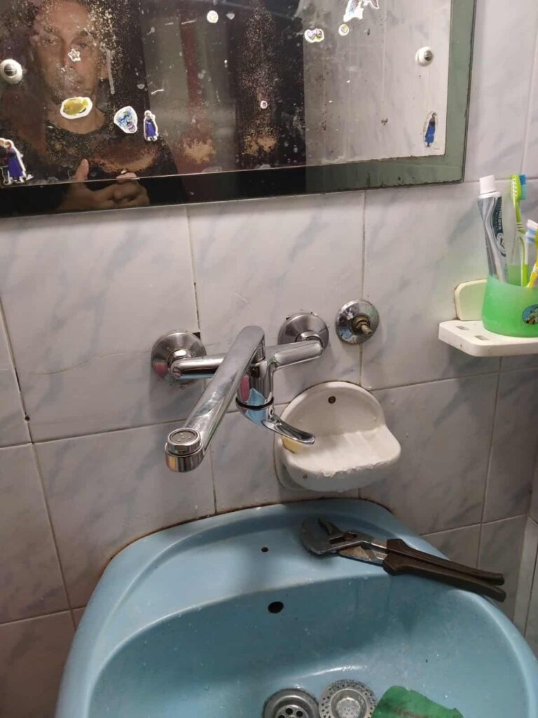 Foto: mlađa muđka osoba fotaografiše sebe u ogledalu neurednog kupatila sa česmom postavljenom naopako